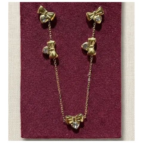 Gold bow jewelry set with matching stud earrings and a delicate chain necklace, each bow adorned with a clear rhinestone, displayed on a burgundy velvet jewelry card.