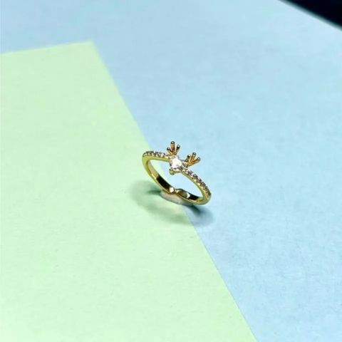 A gold ring with a small deer head motif and a clear center stone, resting on a diagonal split background of light green and light blue.