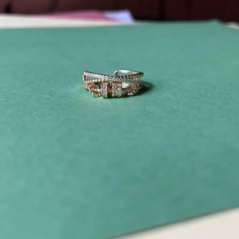 A silver-toned multi-band ring with pavé-set clear stones and rose gold accents, resting on a textured teal-green surface.
